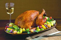 a roasted turkey on a platter with fruit and veggies next to a glass of wine