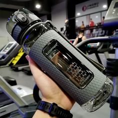 a person holding an electronic device in front of a treadmill at a gym with other equipment