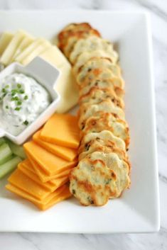 a white plate topped with cheese and crackers next to cucumber, celery