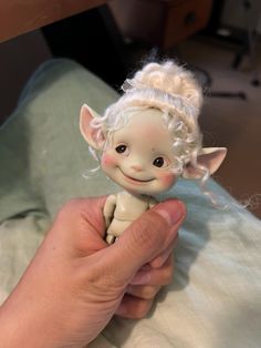 a hand is holding a small doll with white hair on it's head and eyes