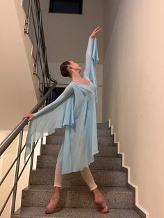 a woman is standing on the stairs with her arms in the air while wearing a blue dress