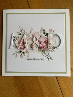 an anniversary card with flowers and the word m & w on it, sitting on a wooden surface