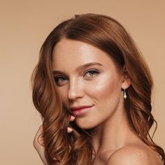 a beautiful young woman with long red hair posing for a photo in front of a beige background