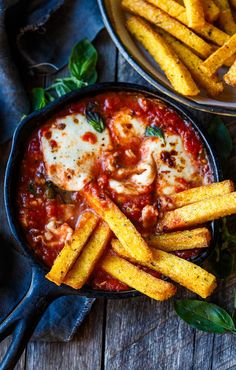 two pans filled with pasta and cheese covered in marinara sauce, on top of a wooden table