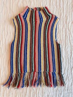 a multicolored striped vest with fringes on the front and back, laying on a bed