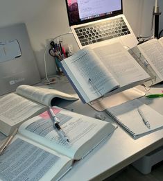 an open laptop computer sitting on top of a desk next to several books and notebooks