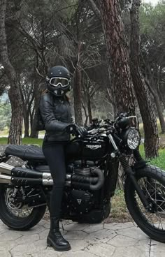 a woman sitting on top of a motorcycle in front of a tree filled park area