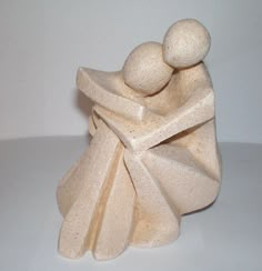 a sculpture of two people hugging each other on a white surface with one holding the other's head