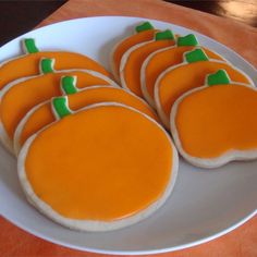 some cookies are on a white plate with orange icing and green decorations in the shape of pumpkins