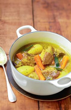 a white bowl filled with stew next to a spoon on top of a wooden table