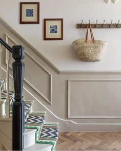 there is a basket hanging on the wall next to some stairs with pictures above it