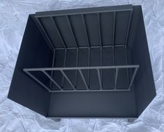 an empty black plastic box on a white sheeted surface with the lid open and metal bars attached to it