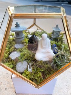 a glass terrarium filled with plants and small buddha figurines sitting on top of it