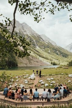 a group of people sitting on top of a wooden bench in front of a mountain