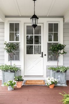 two potted plants are sitting on the front porch next to a white door with glass panes