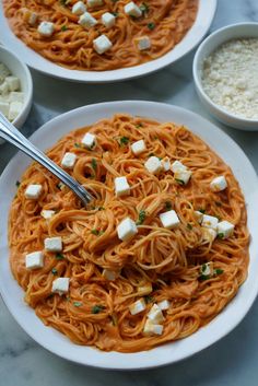 two white plates filled with spaghetti and topped with fettuccine, cheese and parsley