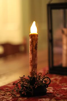 a lit candle sitting on top of a red rug next to a glass container filled with flowers