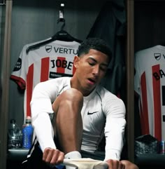 a man sitting on the ground in front of a soccer jersey holding a cup and looking down