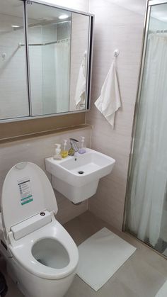 a white toilet sitting next to a sink in a bathroom under a large mirror and shower