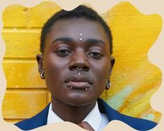 a woman with piercings on her nose standing in front of a yellow brick wall