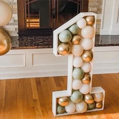 a number one made out of balloons in front of a fireplace with gold and white decorations