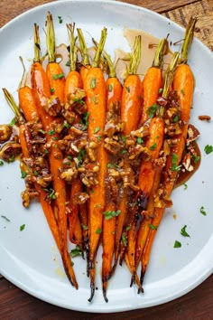 a white plate topped with lots of carrots covered in sauce and chopped up nuts