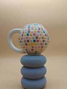 a coffee cup sitting on top of two stacked rocks with a mosaic design on it