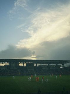 a group of people playing soccer on a field under a blue sky with white clouds