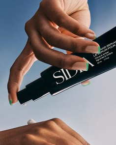 two hands with green and white nail polish on their nails, one holding a black tube