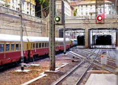 a train traveling through a train station next to tall buildings and traffic lights on poles