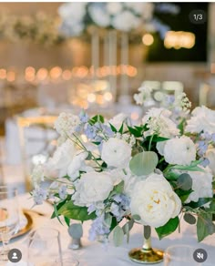 a vase filled with white and blue flowers on top of a table next to wine glasses