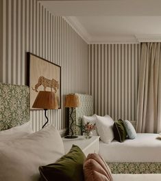 two beds in a room with striped walls and lamps on either side of the bed