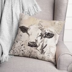 a gray chair with a grey throw pillow on top of it and a black and white cow painting