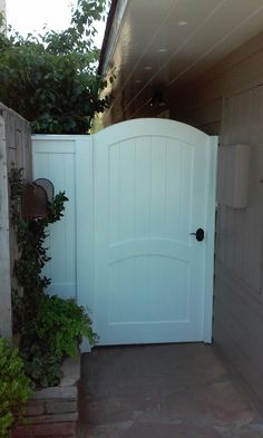 an open white gate in front of a house with plants growing on the outside wall