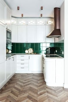 a kitchen with white cabinets and green backsplash tiles on the countertops, along with wood flooring