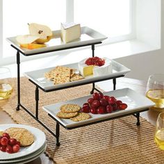 three tiered serving trays with cheese, crackers and fruit on them sitting on a table