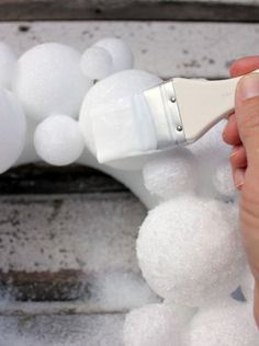 someone using a paint brush to decorate a pom - pom wreath with white balls