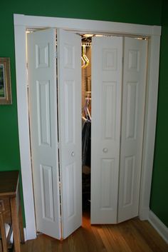 two white doors open in a room with green walls and hardwood floors, along with a wooden table