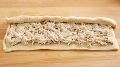 an uncooked pizza dough with shredded chicken on it sitting on a wooden surface