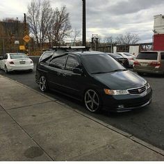 a black car parked on the side of a road next to a parking lot filled with cars