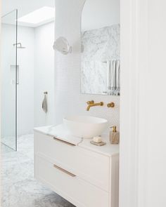 a white bathroom with gold faucet and marble counter tops, along with a walk in shower