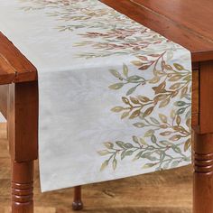 a wooden table topped with a white table cloth covered in leafy designs on it