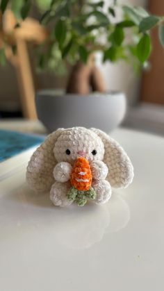 a crocheted bunny holding a carrot in its mouth on a table next to a potted plant