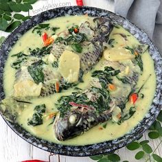 a bowl filled with fish and vegetables on top of a wooden table next to green leaves