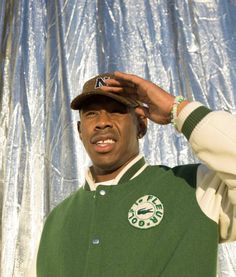 a man in a green jacket and hat with his hand on the top of his head