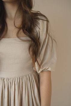 a woman with long brown hair wearing a white dress and holding her hands in her pockets