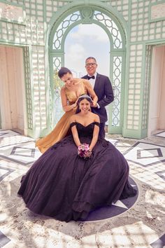 two men and a woman in formal wear posing for a photo on the ground with an archway behind them