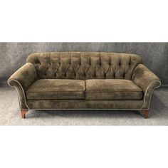 a brown velvet couch with wooden legs and buttons on the back, in front of a gray wall