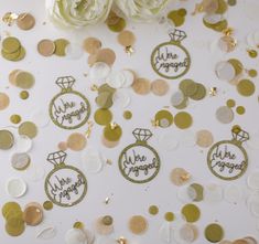 gold and white confetti with we are engaged stickers next to some flowers