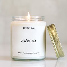 a candle that is sitting next to a container with a lid on it and the words bridesmaid written in black